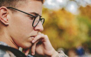 Photo of a young teen or adult male profile face who appears to be reading or thinking. Hes wearing glasses, and has his chin resting on one hand.