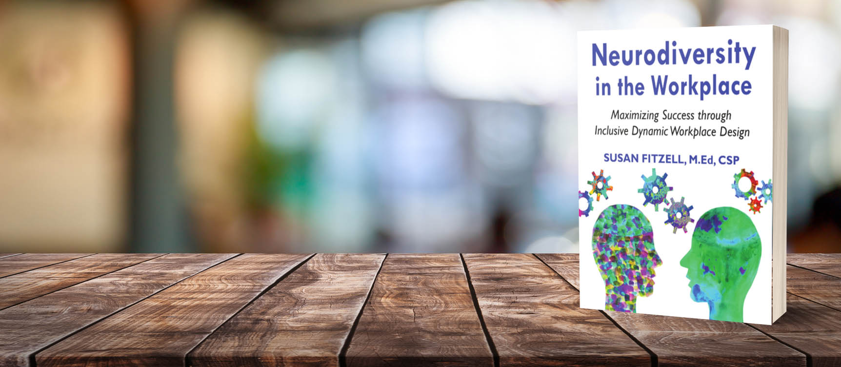 Book cover titled “Neurodiversity in the Workplace: Maximizing Success through Inclusive Dynamic Workplace Design” by Susan Fitzell displayed upright on a wooden table, with a softly blurred office background, suggesting a professional workplace setting.